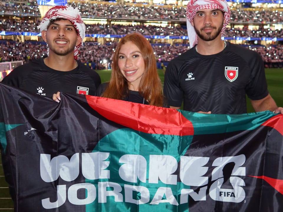 Faris and friends in Jordan kits holding a We Are Jordan flag in a packed stadium