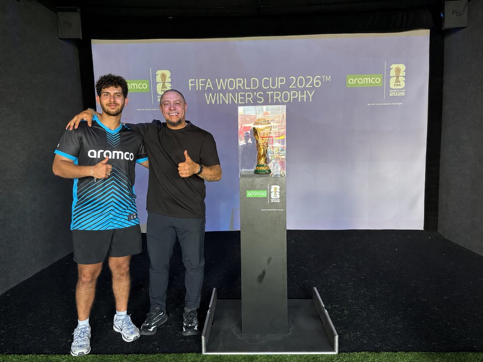 Faris giving a thumbs-up next to Roberto Carlos and the FIFA World Cup trophy